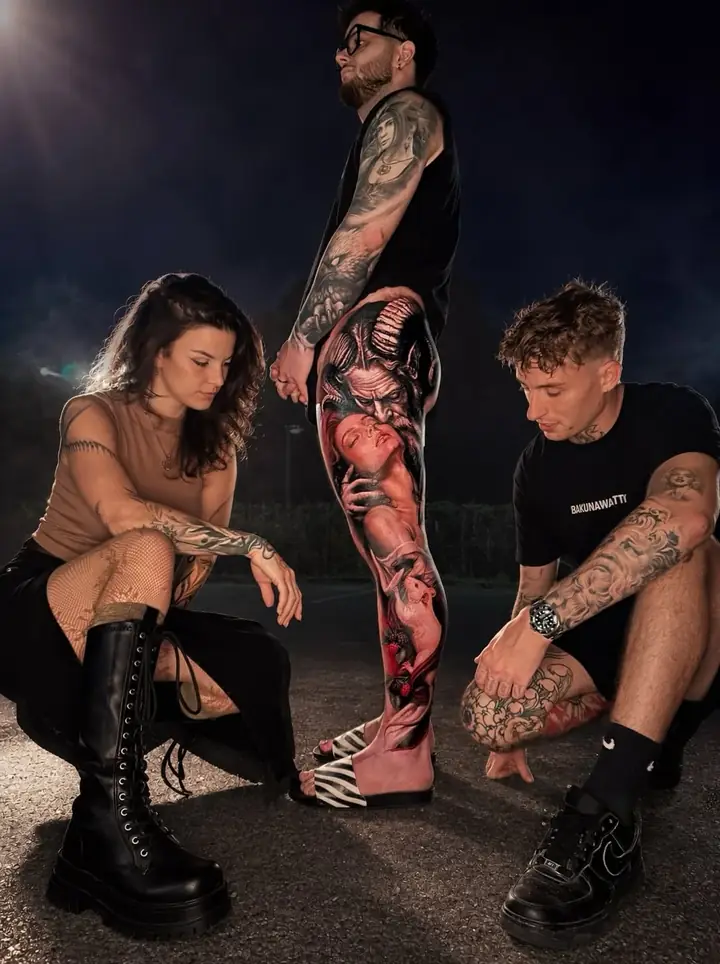 Photo de nuit : trois personnes tatouées autour d’un tatouage réaliste sur une jambe